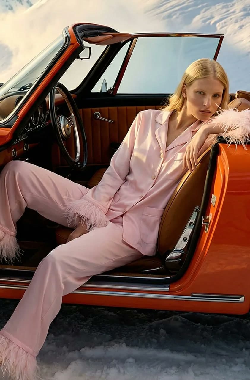 AI model in a pink feather-trimmed set, in an orange classic car