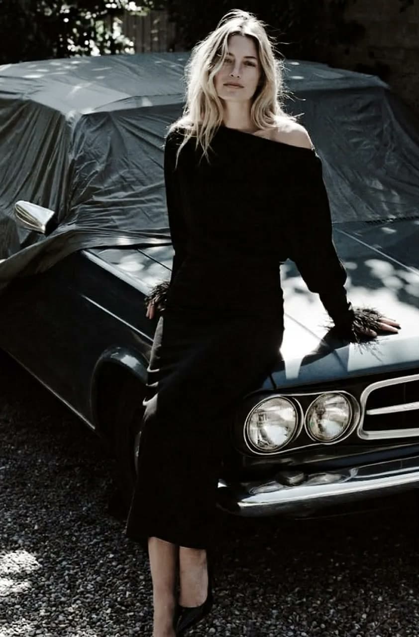 AI model in a black dress, leaning on a classic car
