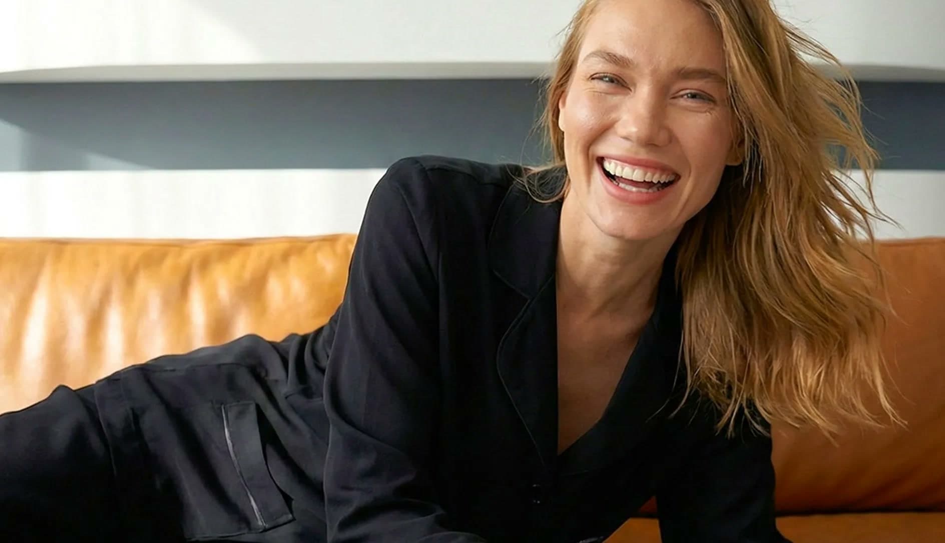 Model in a black satin set, laughing on a leather sofa